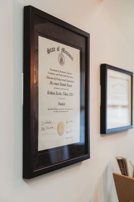Two framed diplomas on a white wall. One is larger, with text and a seal. The frames are black.