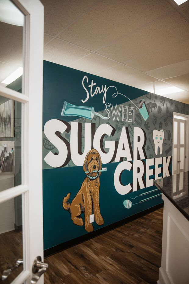 Mural at Sugar Creek Dental: large dog, white text, teal wall. Open doorway and counter are visible.