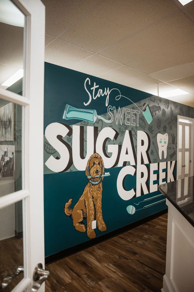 Mural at Sugar Creek Dental: large dog, white text, teal wall. Open doorway and counter are visible.
