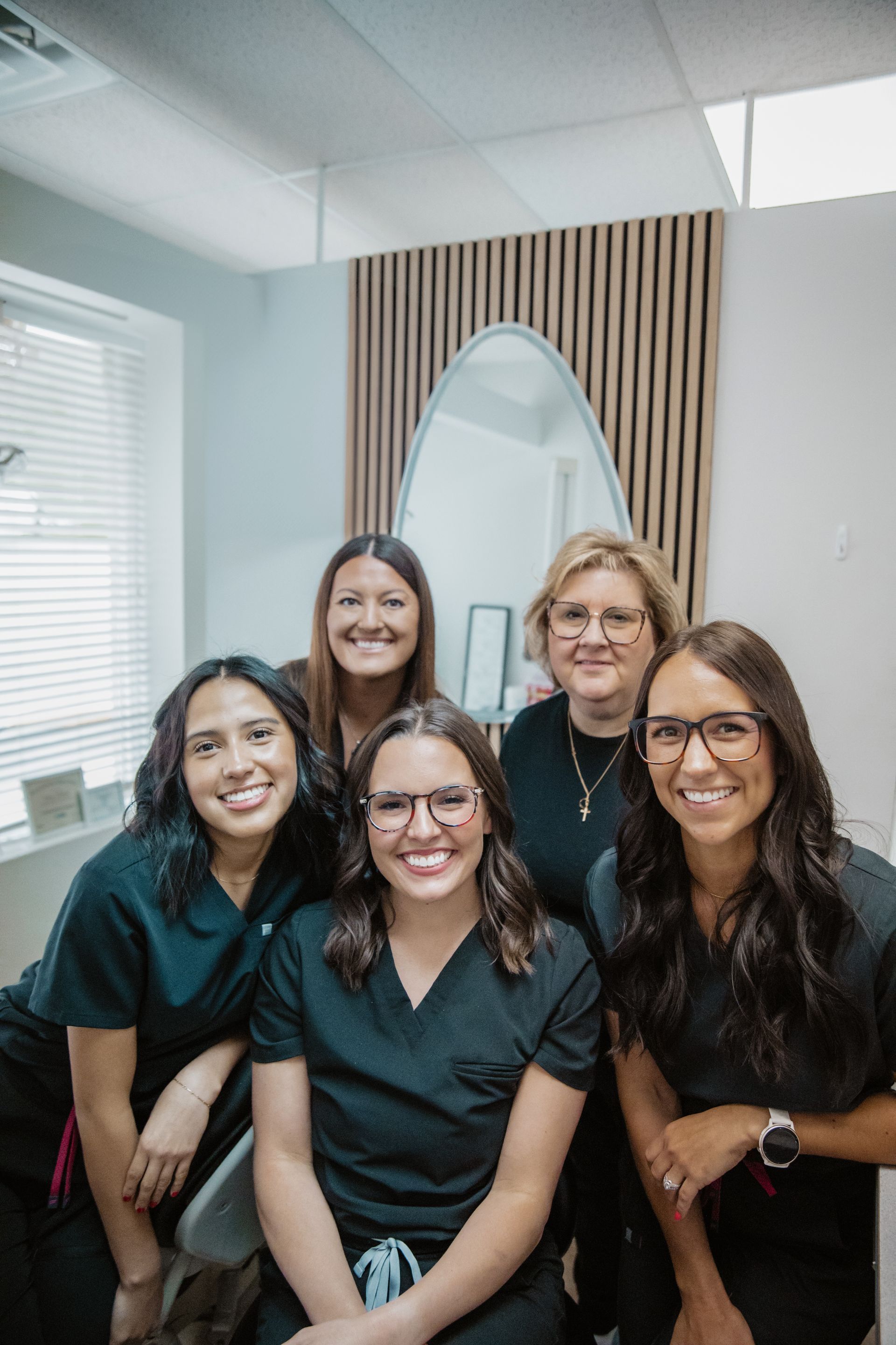 Five smiling people in black tops pose together in a light-filled office.