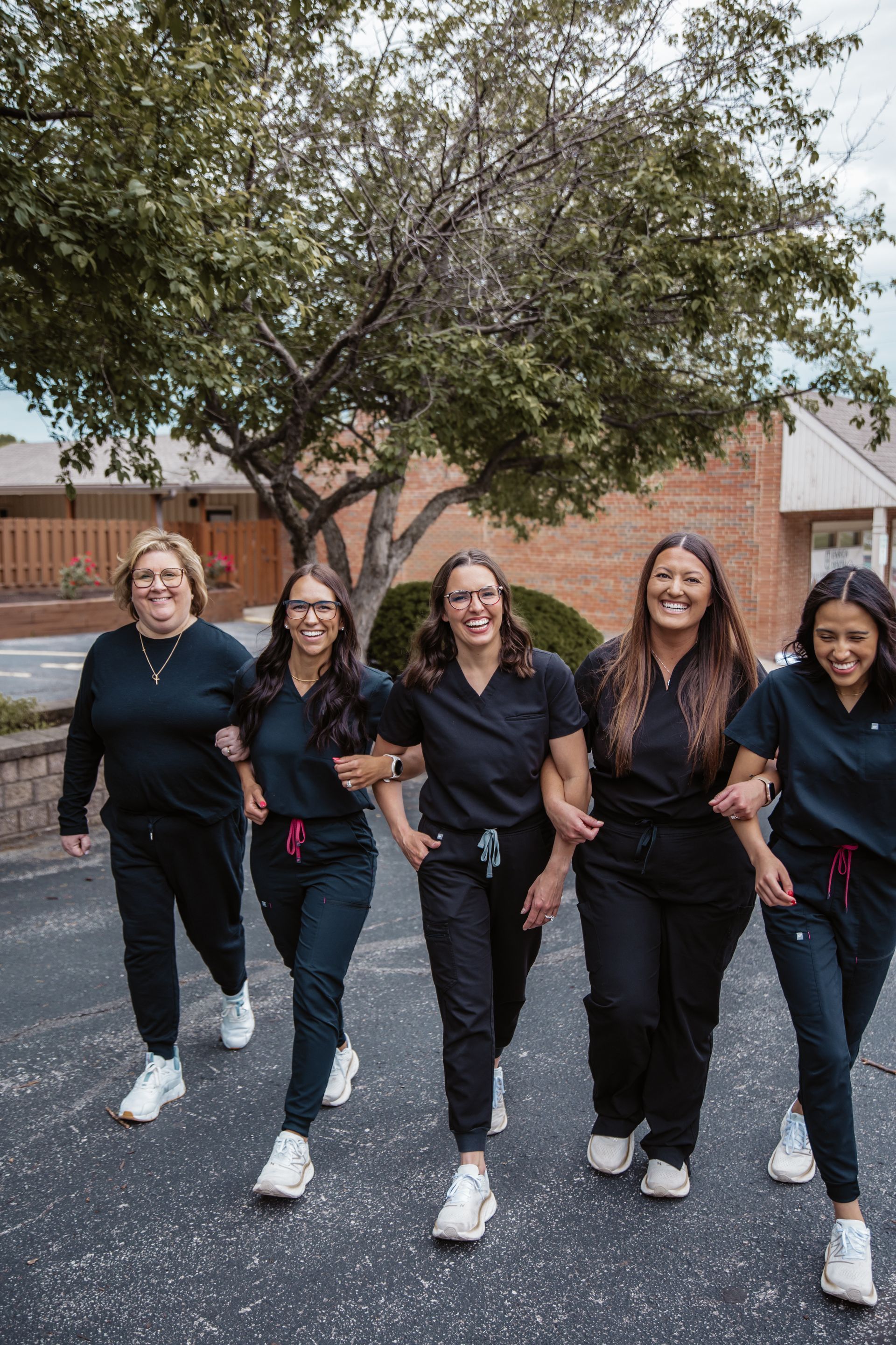 Five people in dark scrubs walk arm in arm outside, smiling.