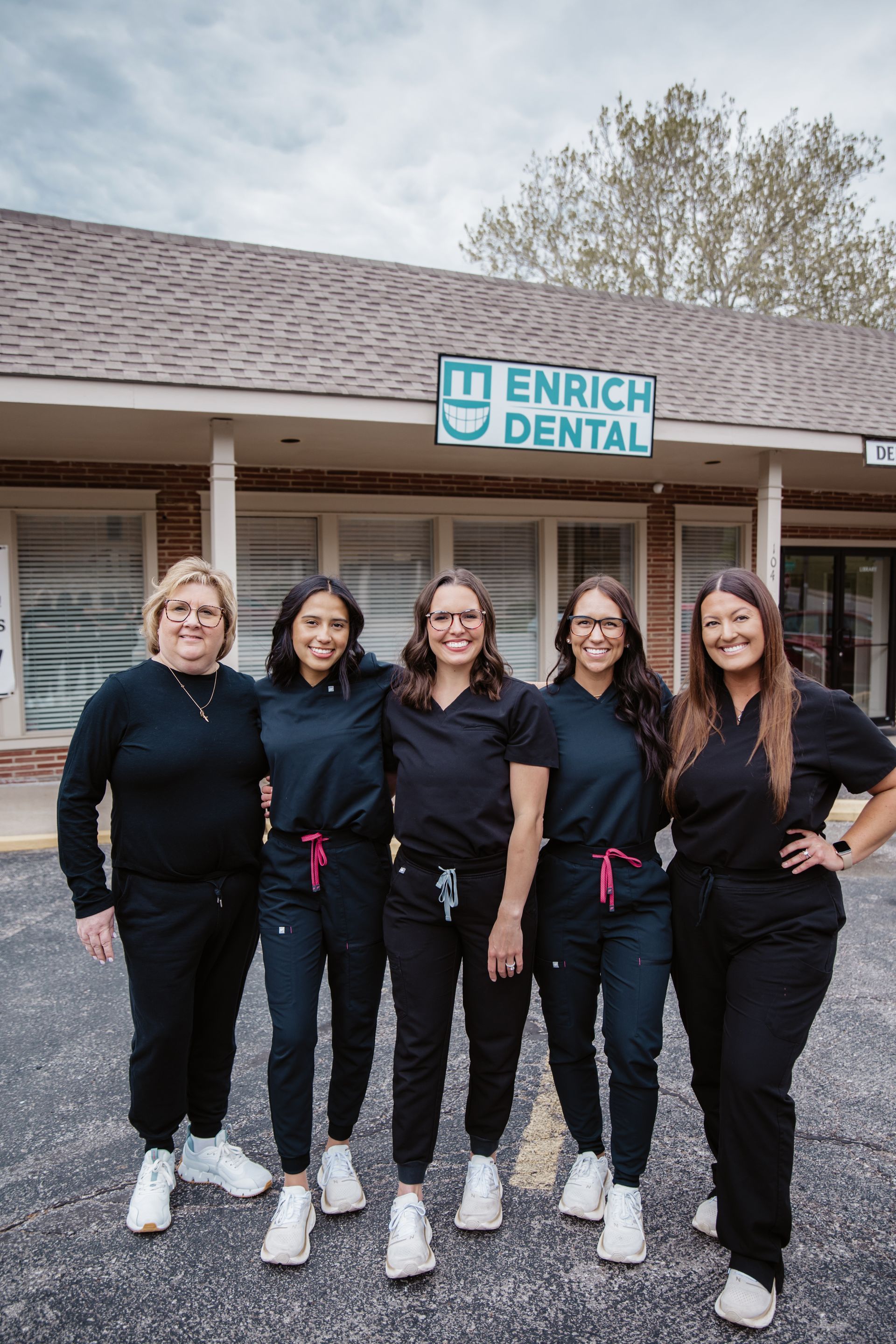 Five dental staff members in black scrubs pose in front of the Enrich Dental office.