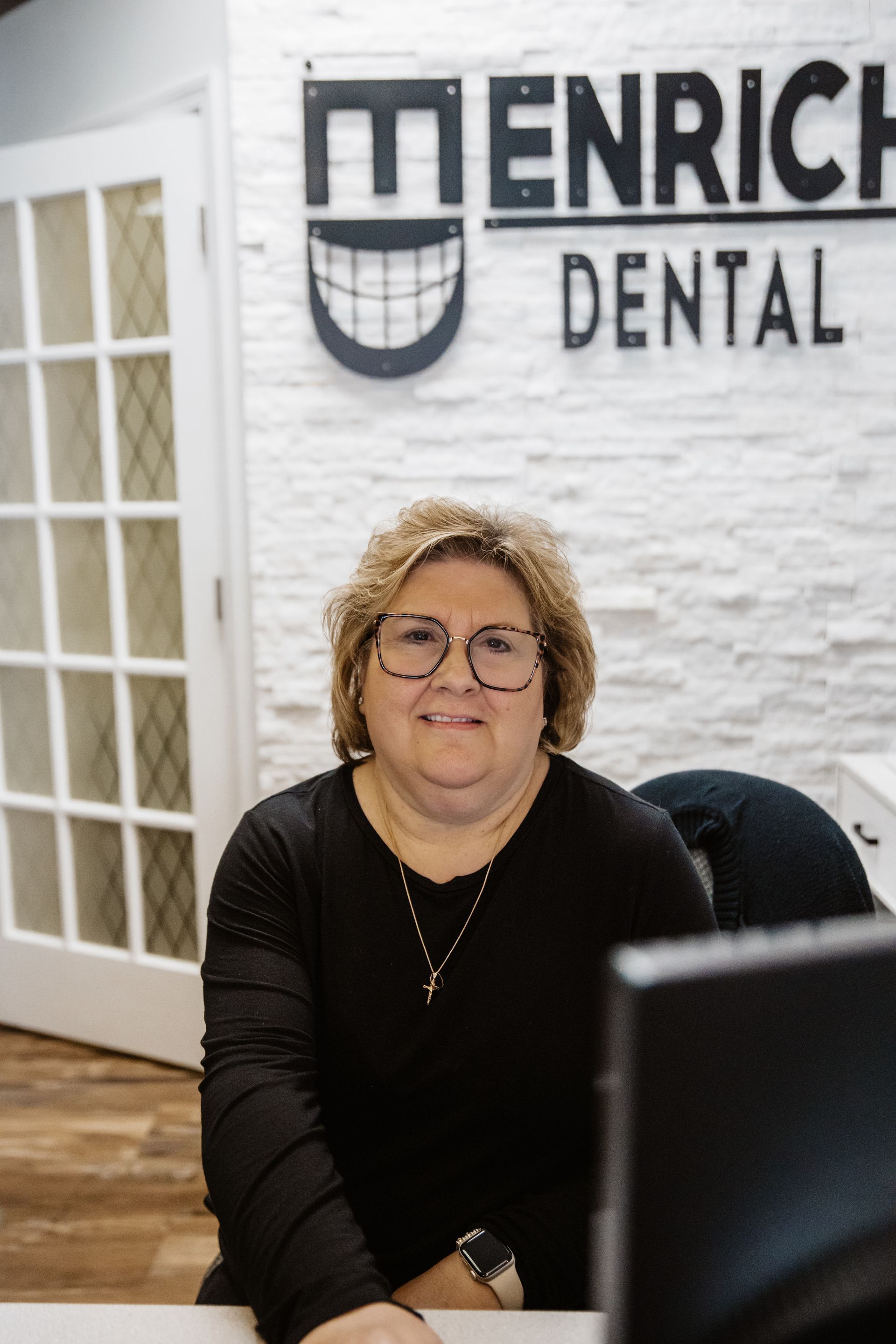 Woman in glasses, black shirt, in front of 