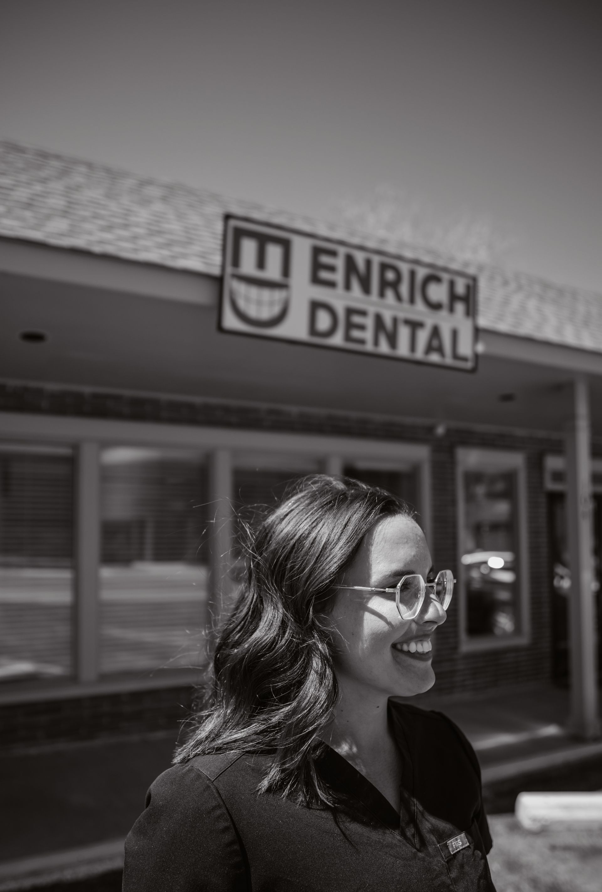 Woman smiling in front of a dental office sign, 