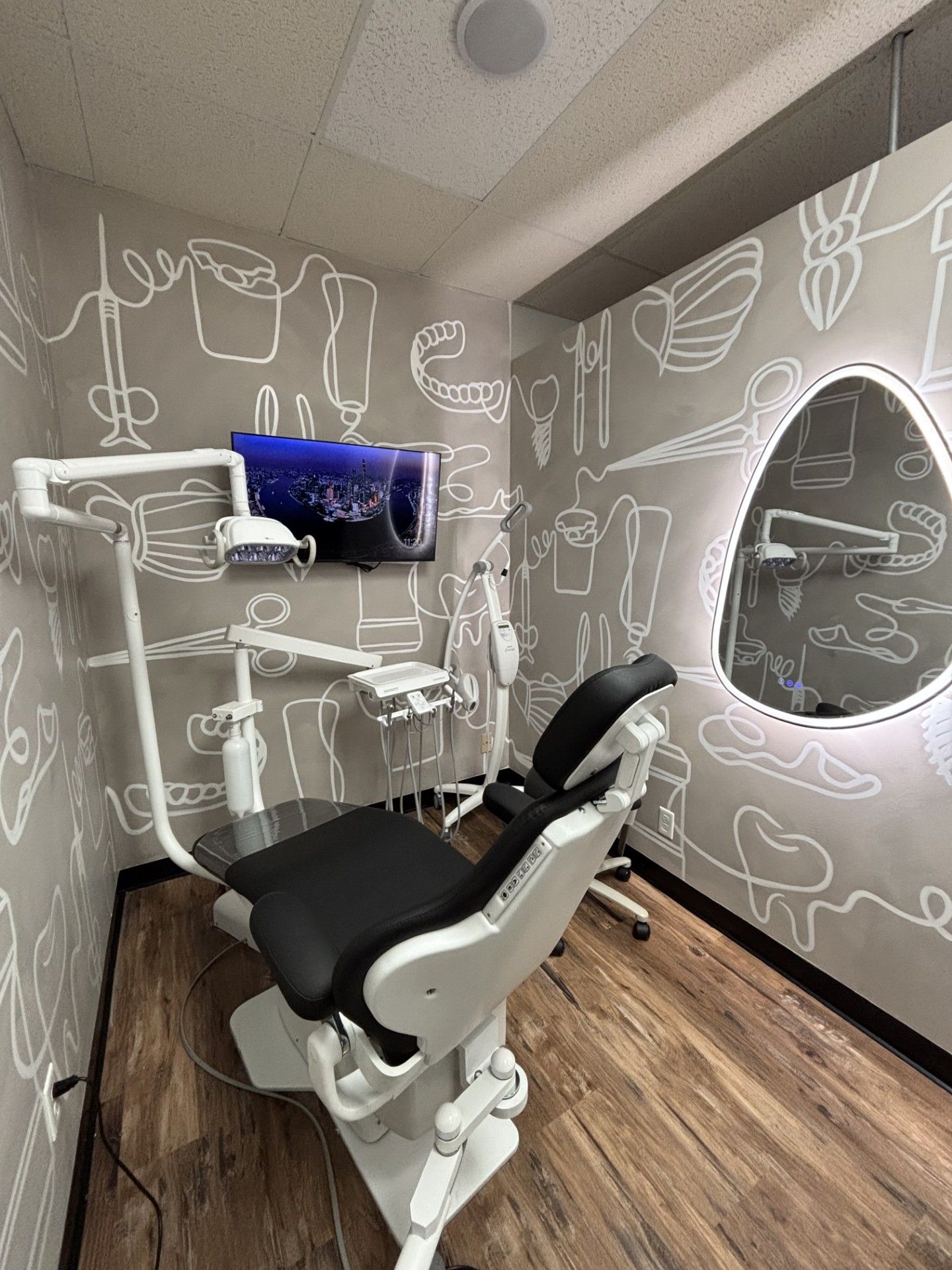 Dental exam room with a black and white chair, tools, mirror, and a wall-mounted TV.