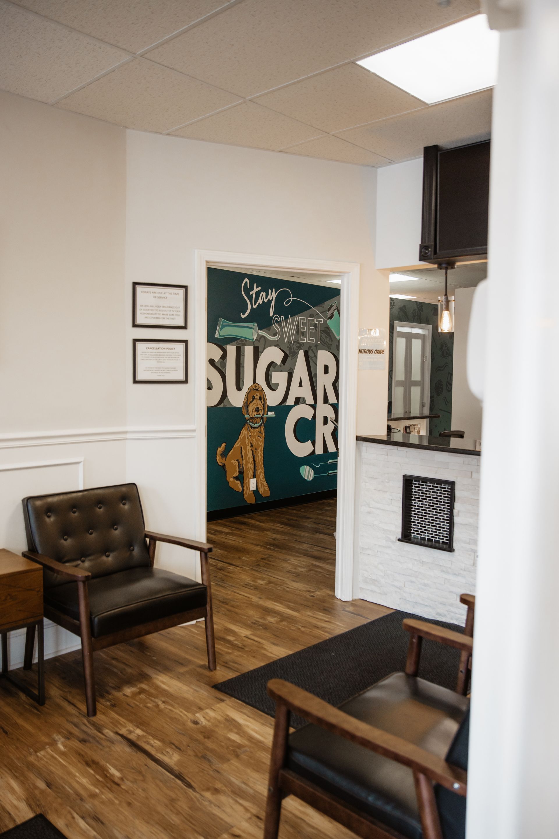Waiting room with two chairs, wooden floors, and a view into an office with a mural.