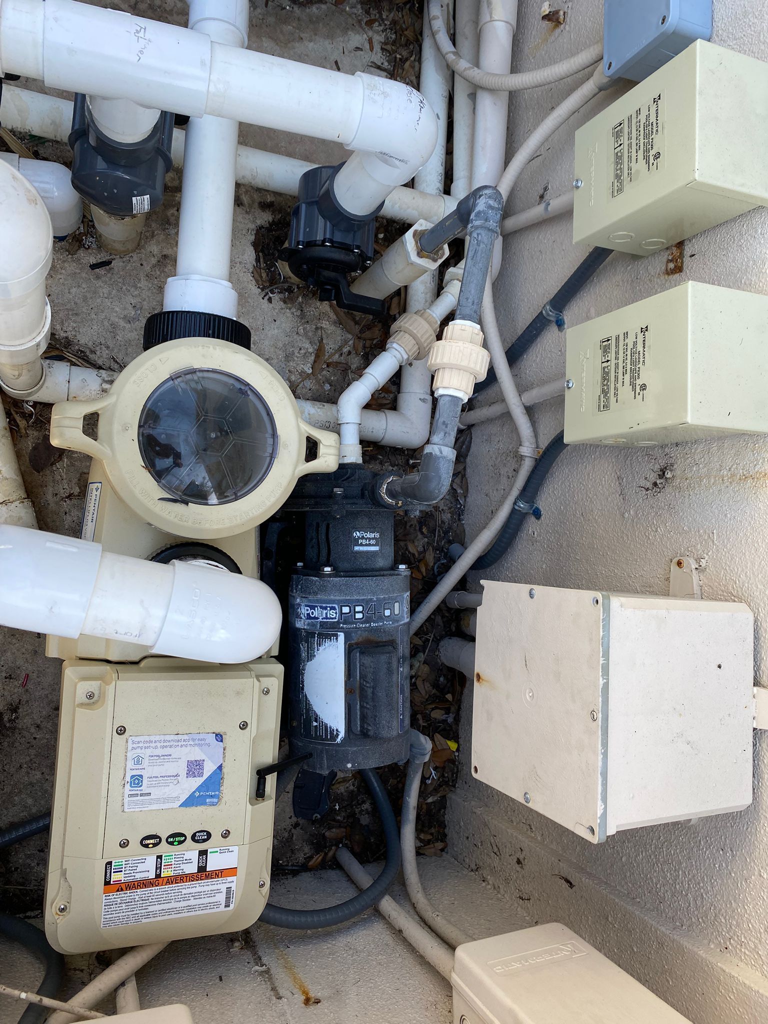 Pool pump system with white PVC pipes, electrical boxes, and a black pump.