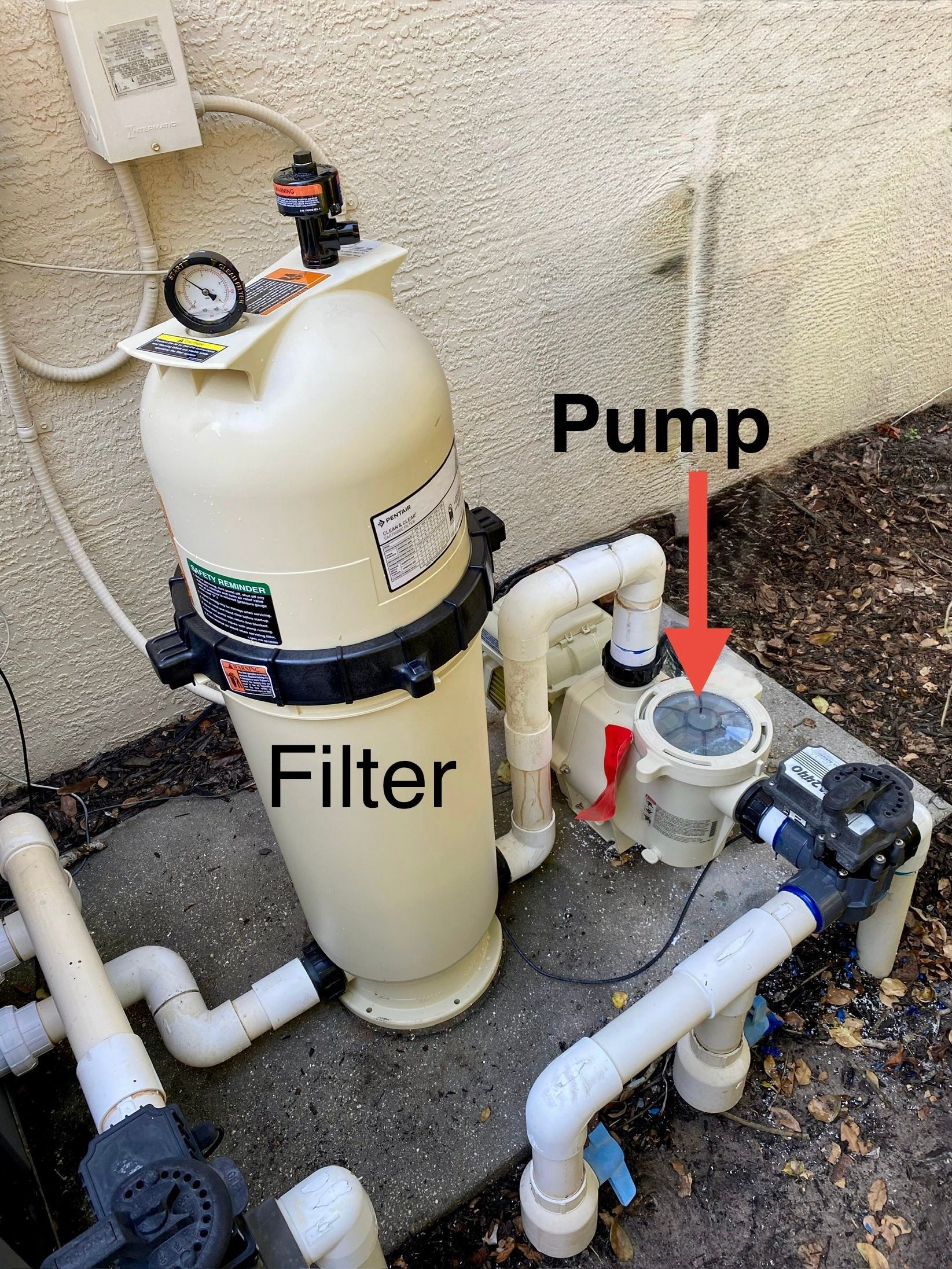 Pool filter and pump system, with a beige filter, white pipes, and a blue valve outdoors.