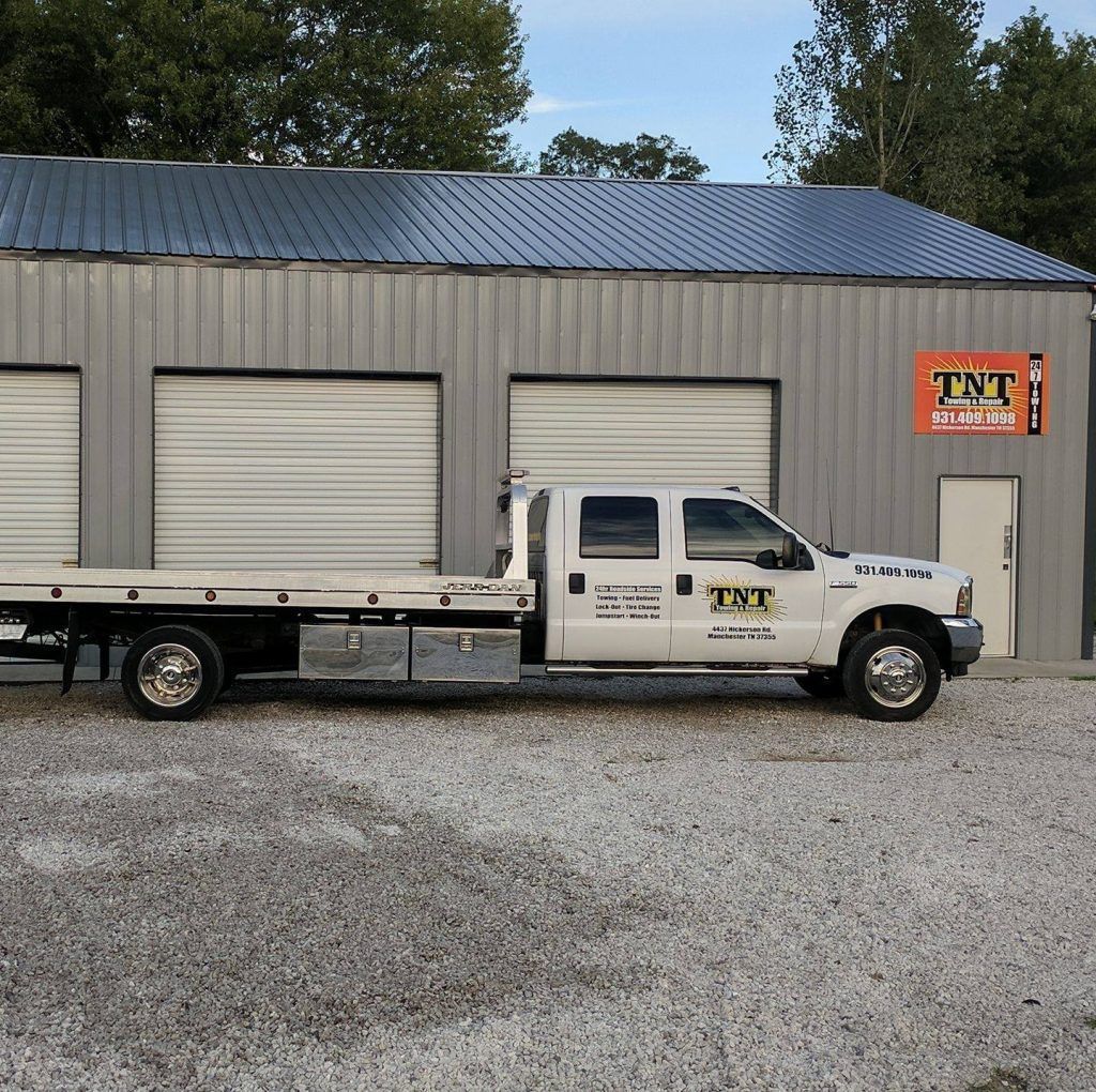 White TNT truck parked outside a gray warehouse with roll-up doors and orange TNT sign