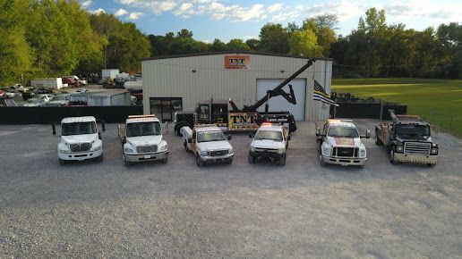 Seven utility trucks parked in front of a white building on a gravel lot.