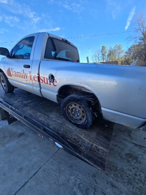 Silver pickup truck with red business lettering parked on a driveway in bright sunlight