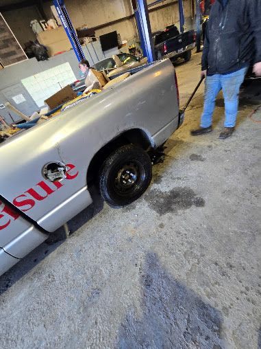 Silver pickup truck in a workshop, with a person standing beside it on a wet floor.