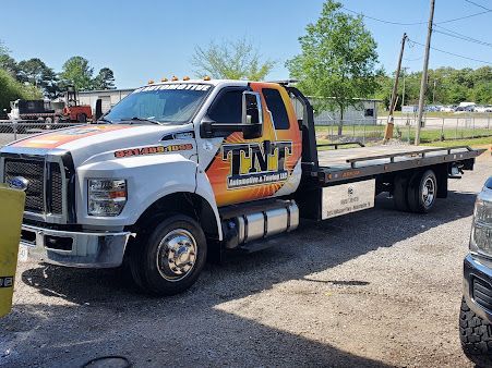 White tow truck with orange TNT logo parked on a street under a clear sky