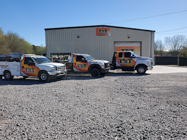 Three branded service vans parked in front of a gray metal building on a gravel lot.