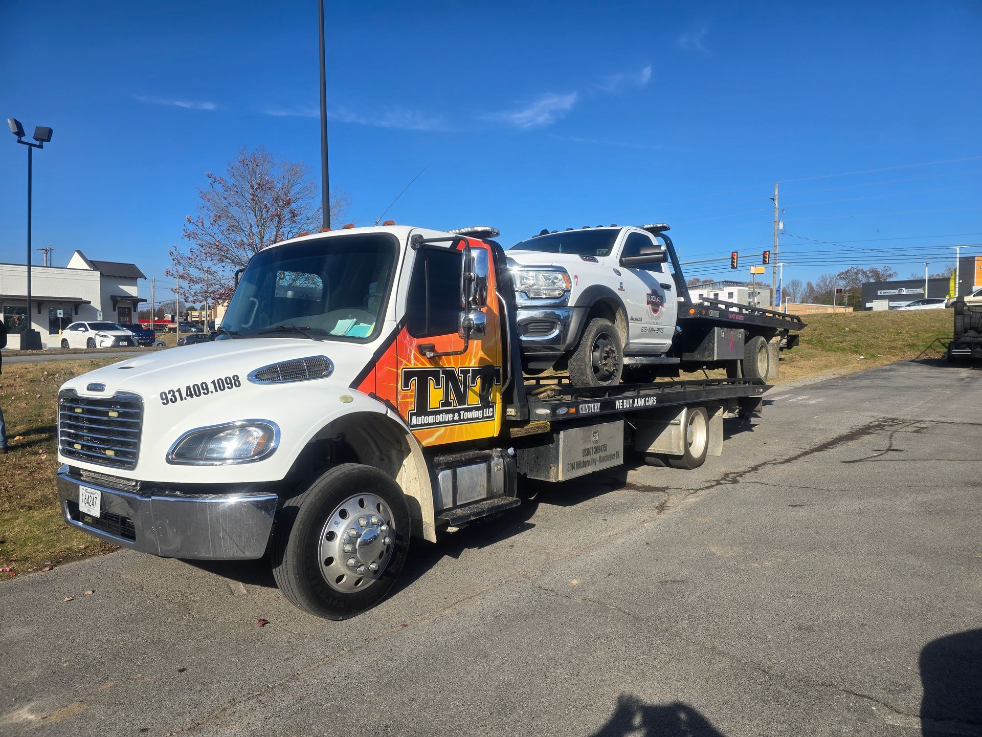 White tow truck carrying a silver SUV on a flatbed under a clear blue sky.