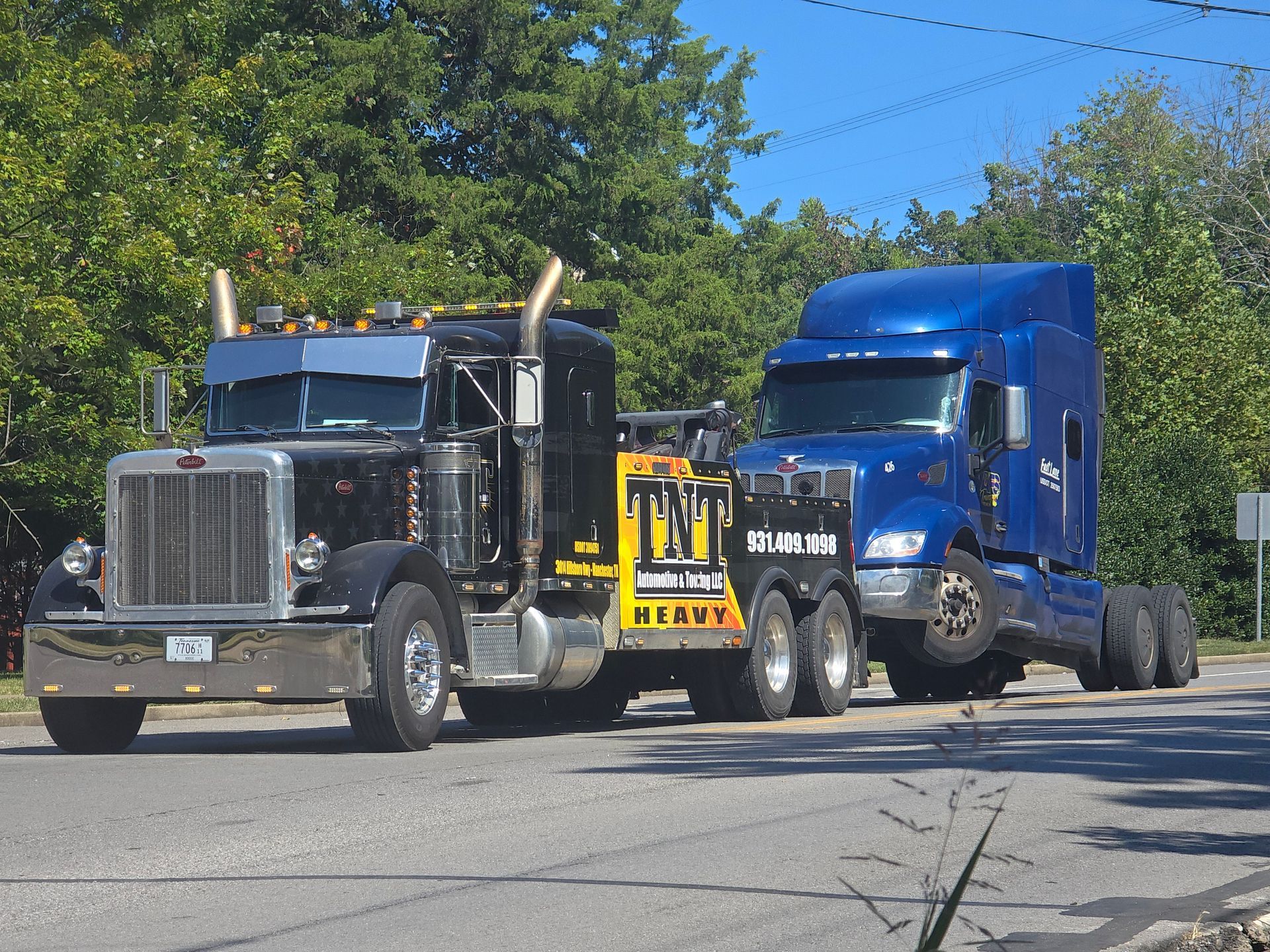 Black and blue semi trucks parked side by side on a sunny street.