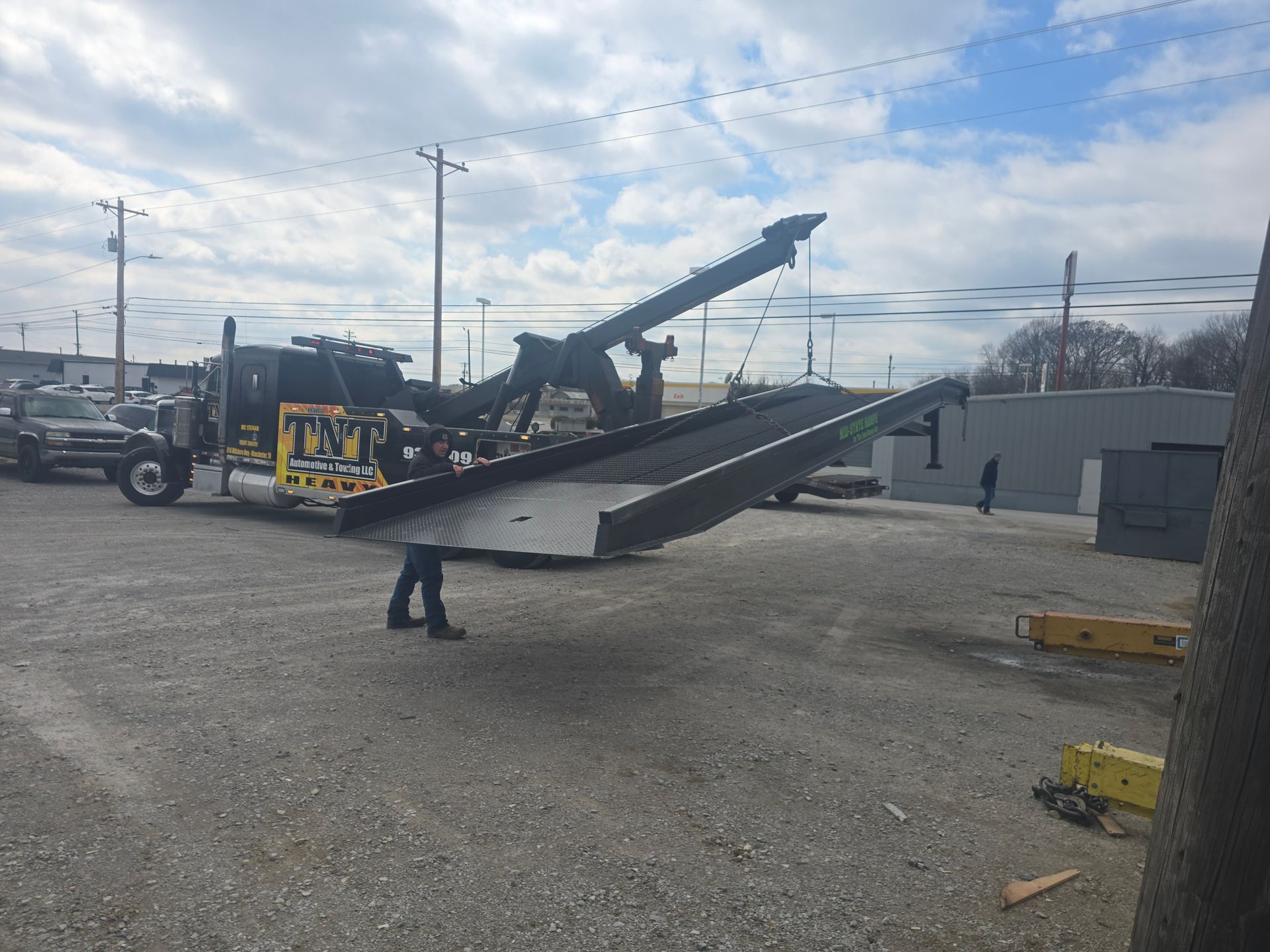 Low-profile car hauler ramp loaded with equipment in an industrial lot under cloudy skies.