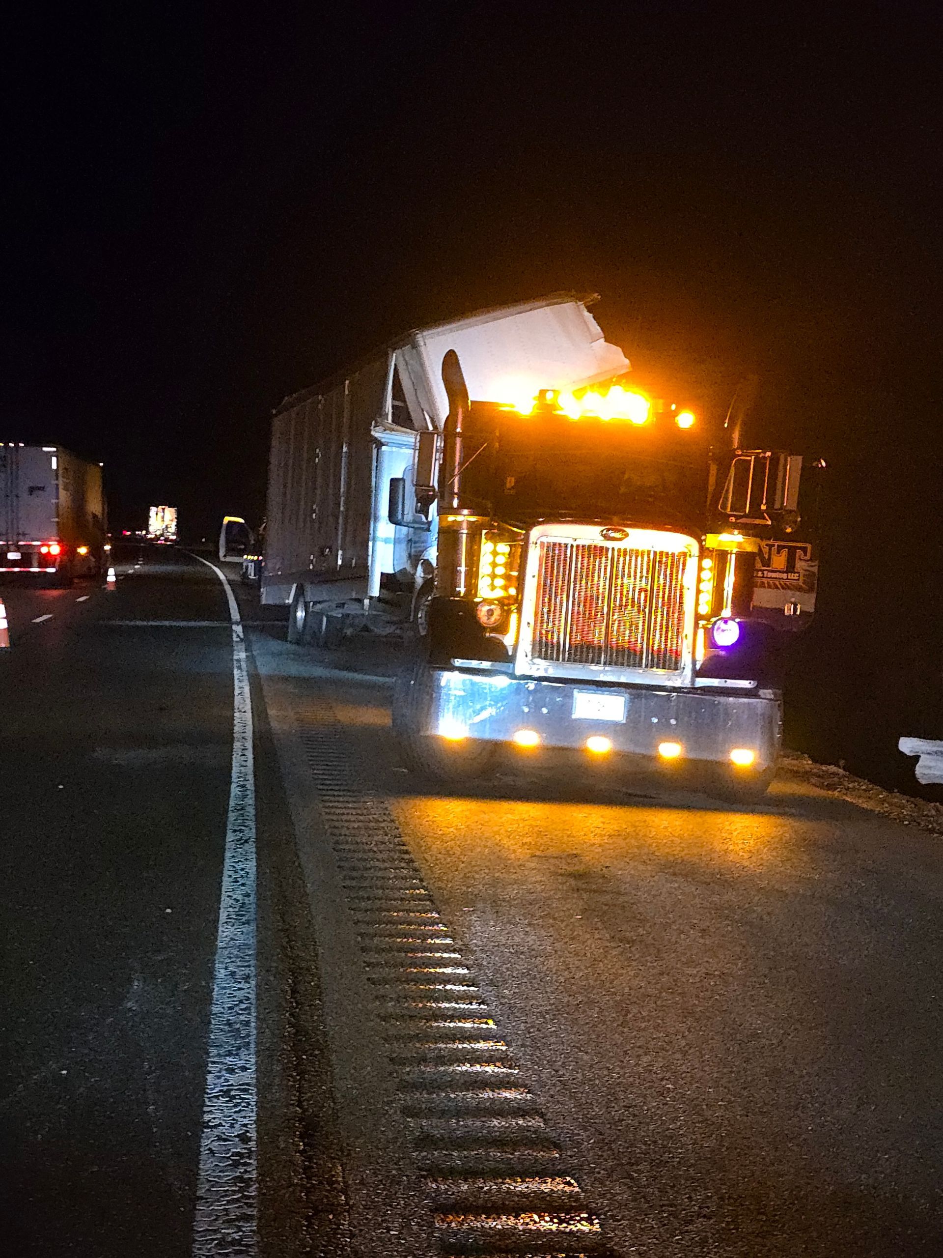 Brightly lit semi truck on a dark highway at night, with headlights and orange marker lights shining.