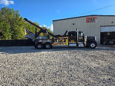 Black utility truck with yellow lift parked on gravel outside a warehouse under a blue sky