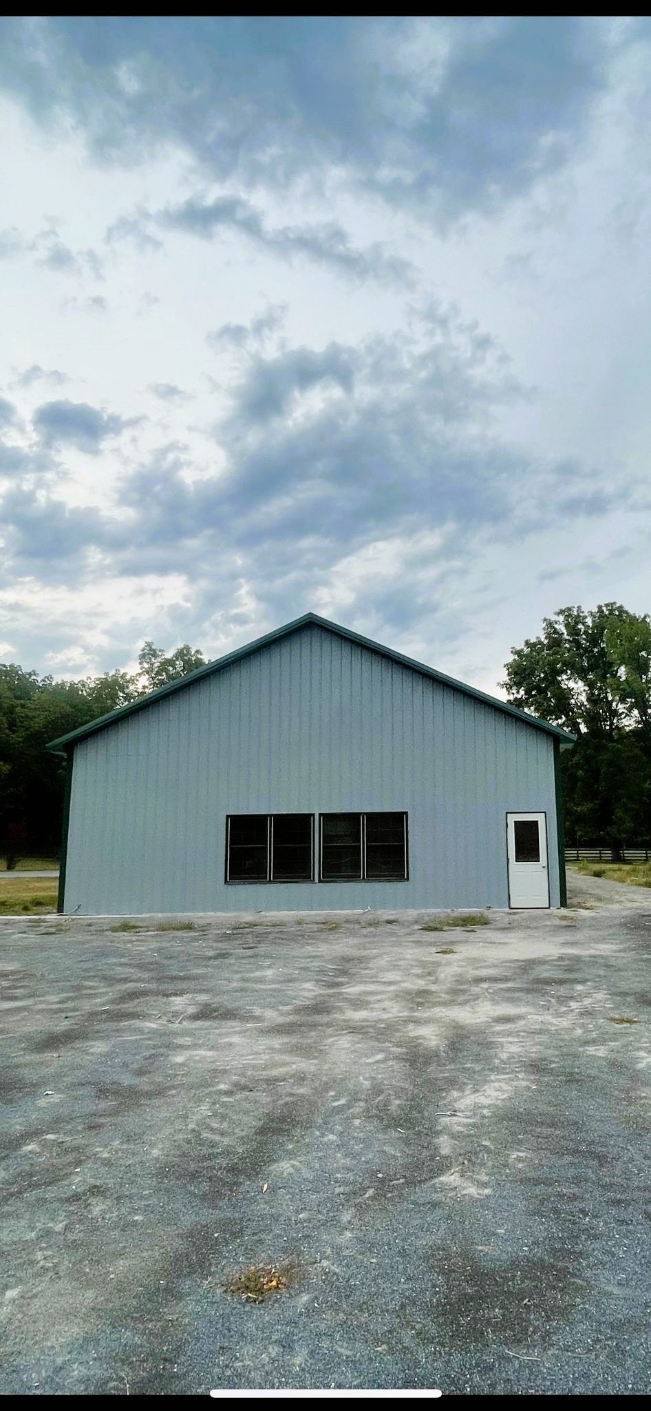 A light blue metal building with a white door, set on a gravel lot under a cloudy sky.