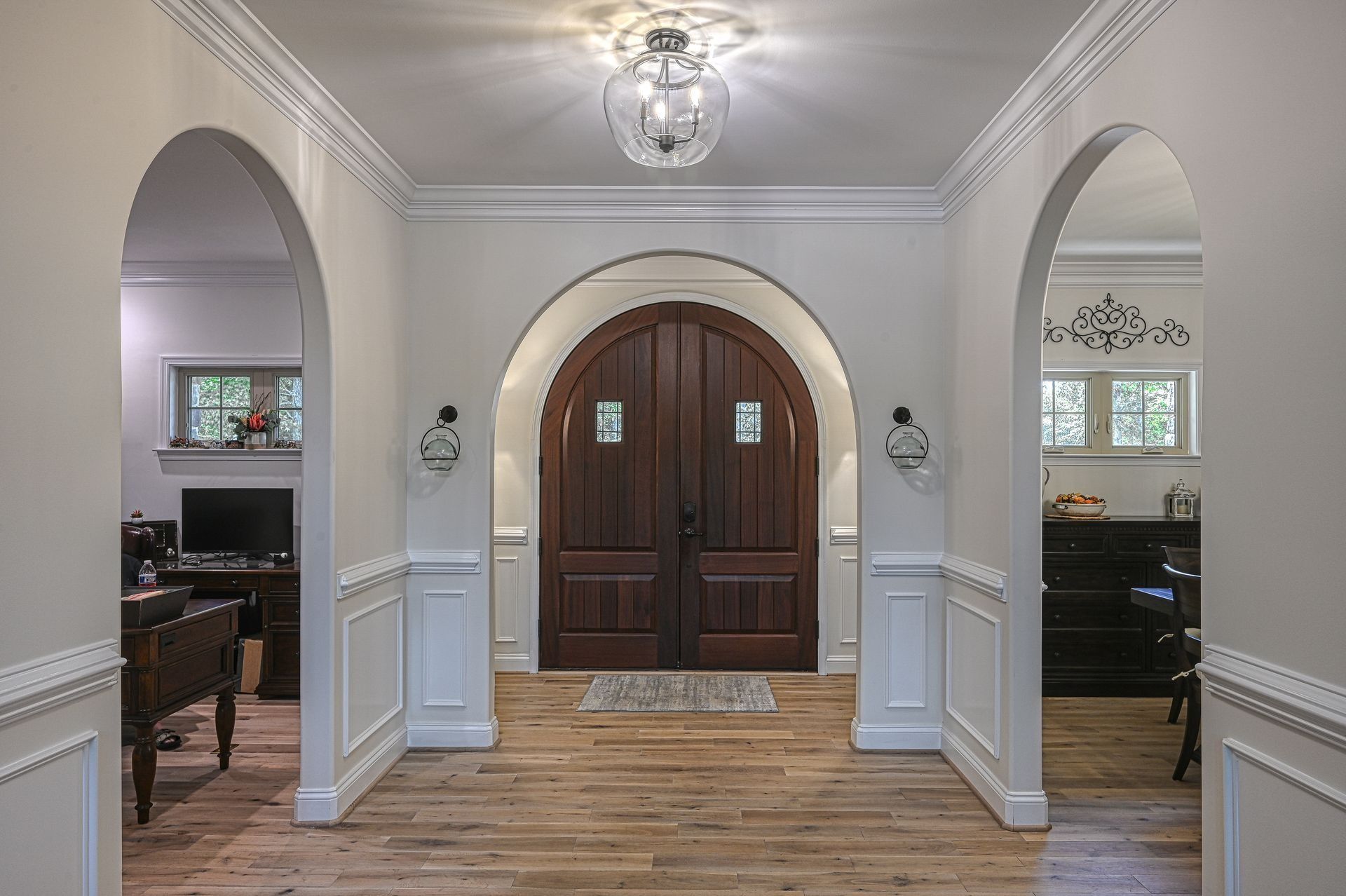 Hallway with arched doorways, wood doors, crown molding, and hardwood floors.