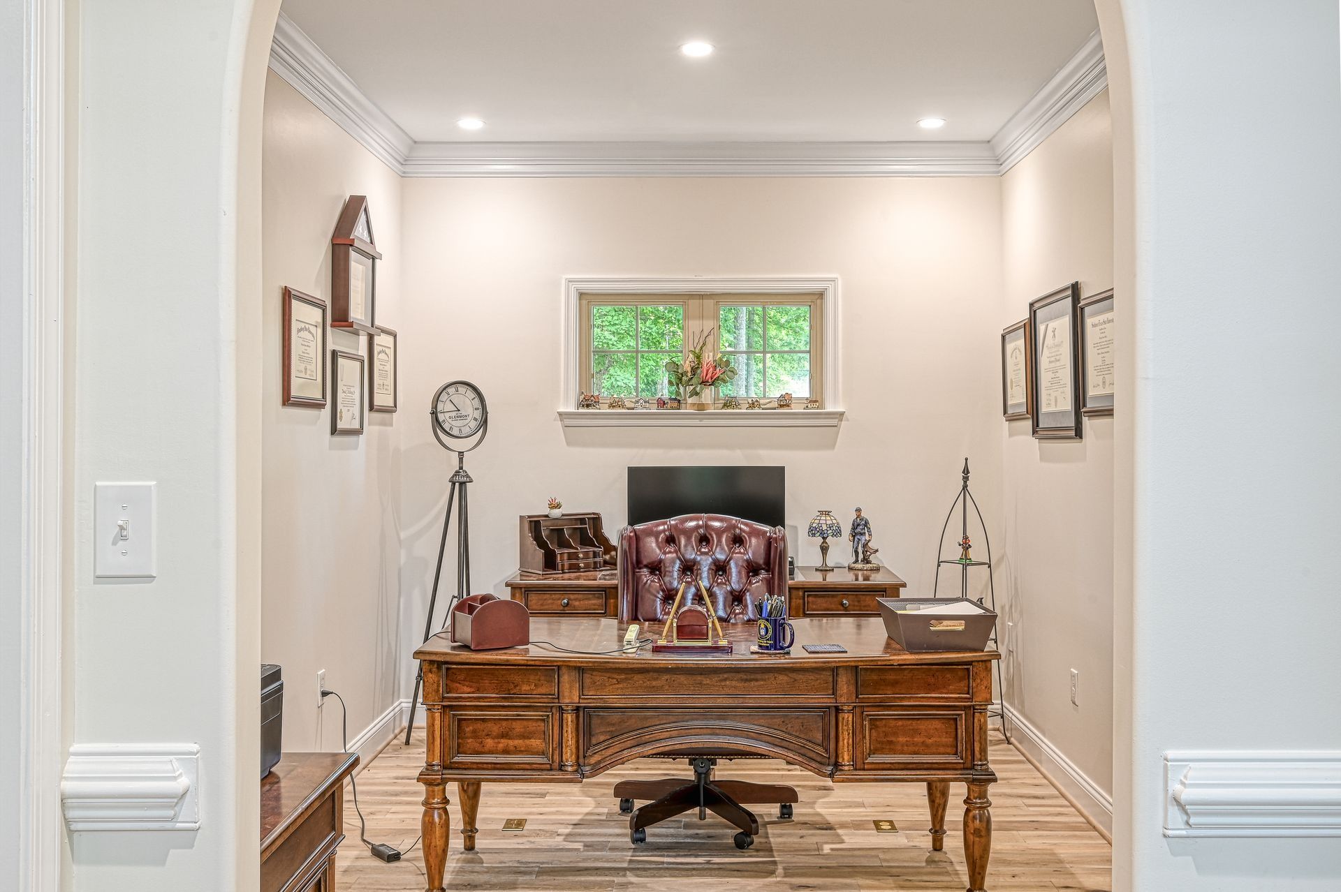 Ornate wooden home office with desk, chair, and decor, viewed through a doorway.