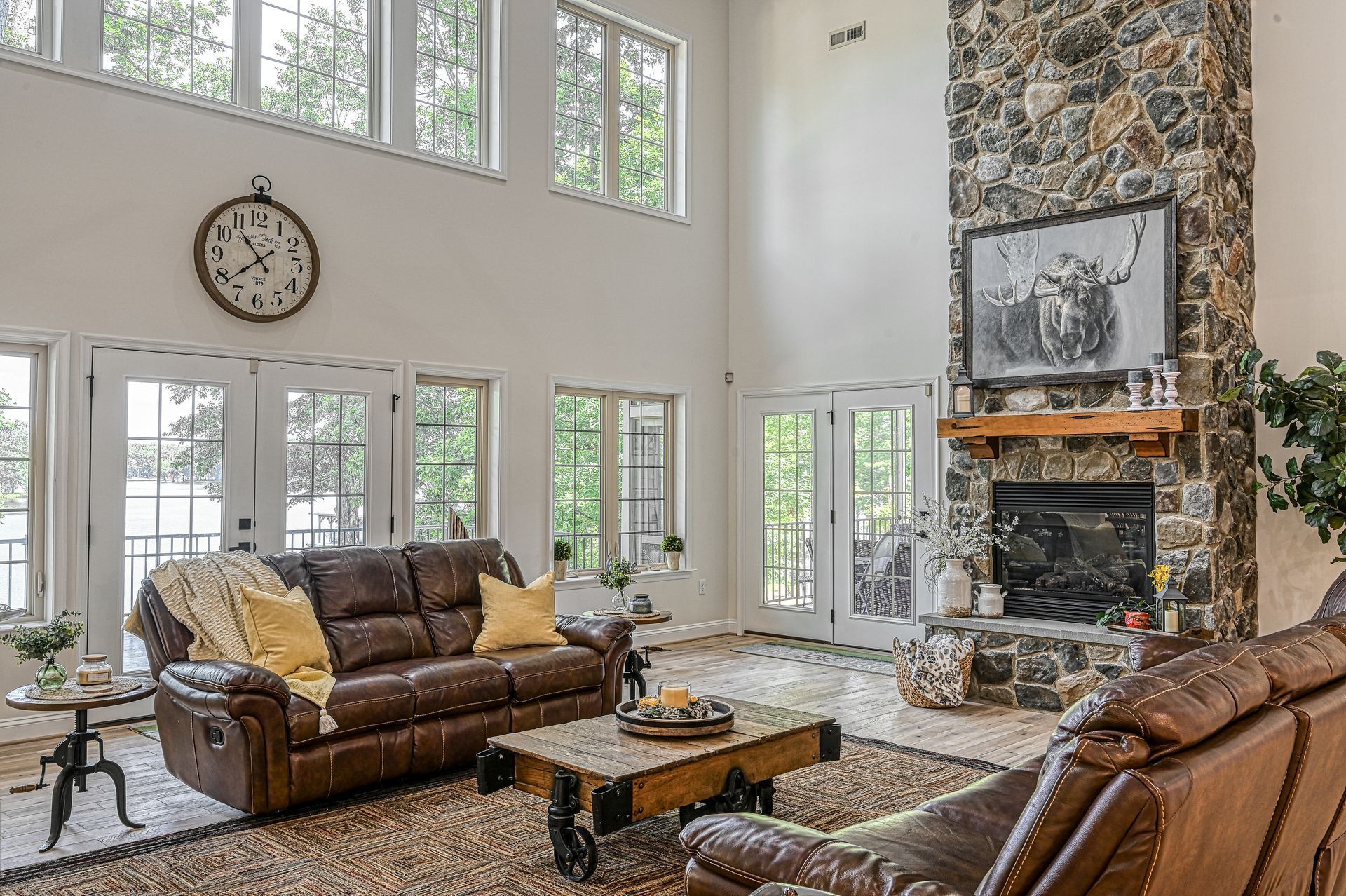 Spacious living room with stone fireplace, leather sofas, large windows, and an antique clock.