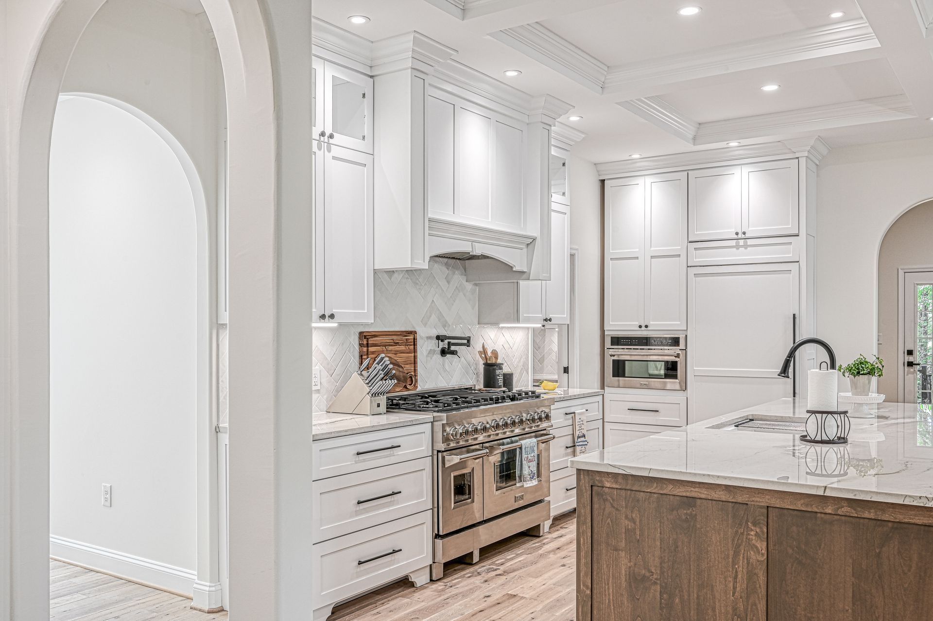 White kitchen with stainless steel appliances, marble backsplash, and wooden island.