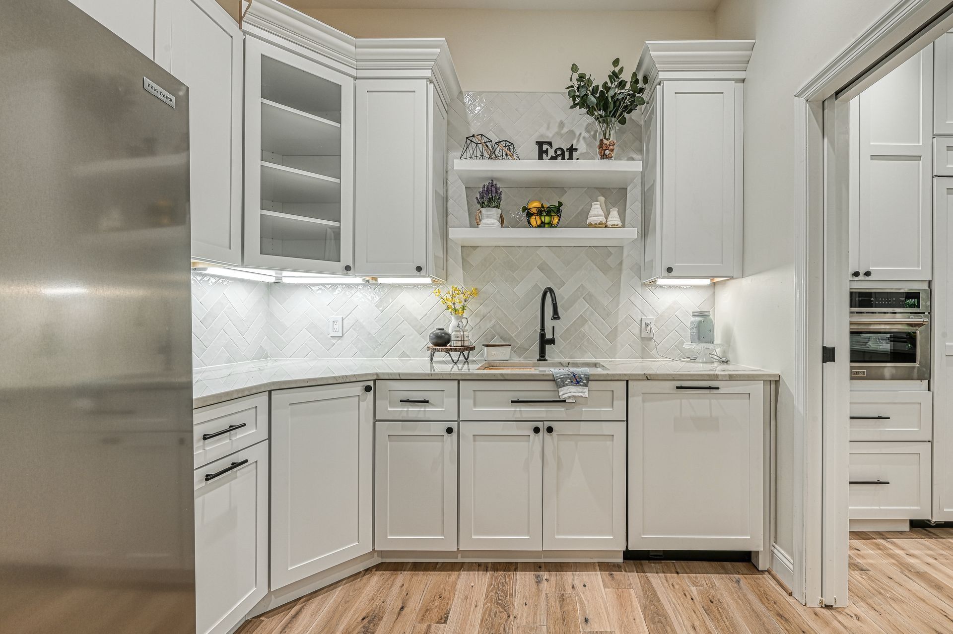 White kitchen with cabinets, stainless steel refrigerator, and wooden floors.