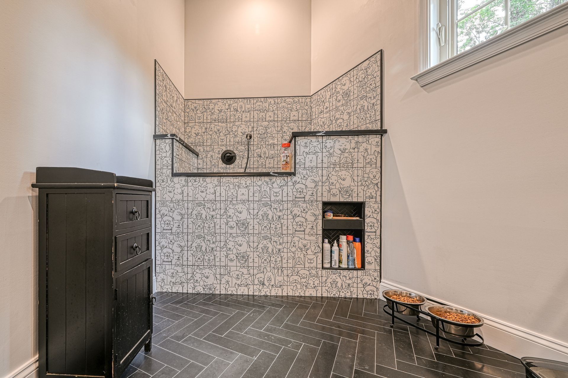 Bathroom with black and white tile shower, built-in shelf, black cabinet, and dark floor.