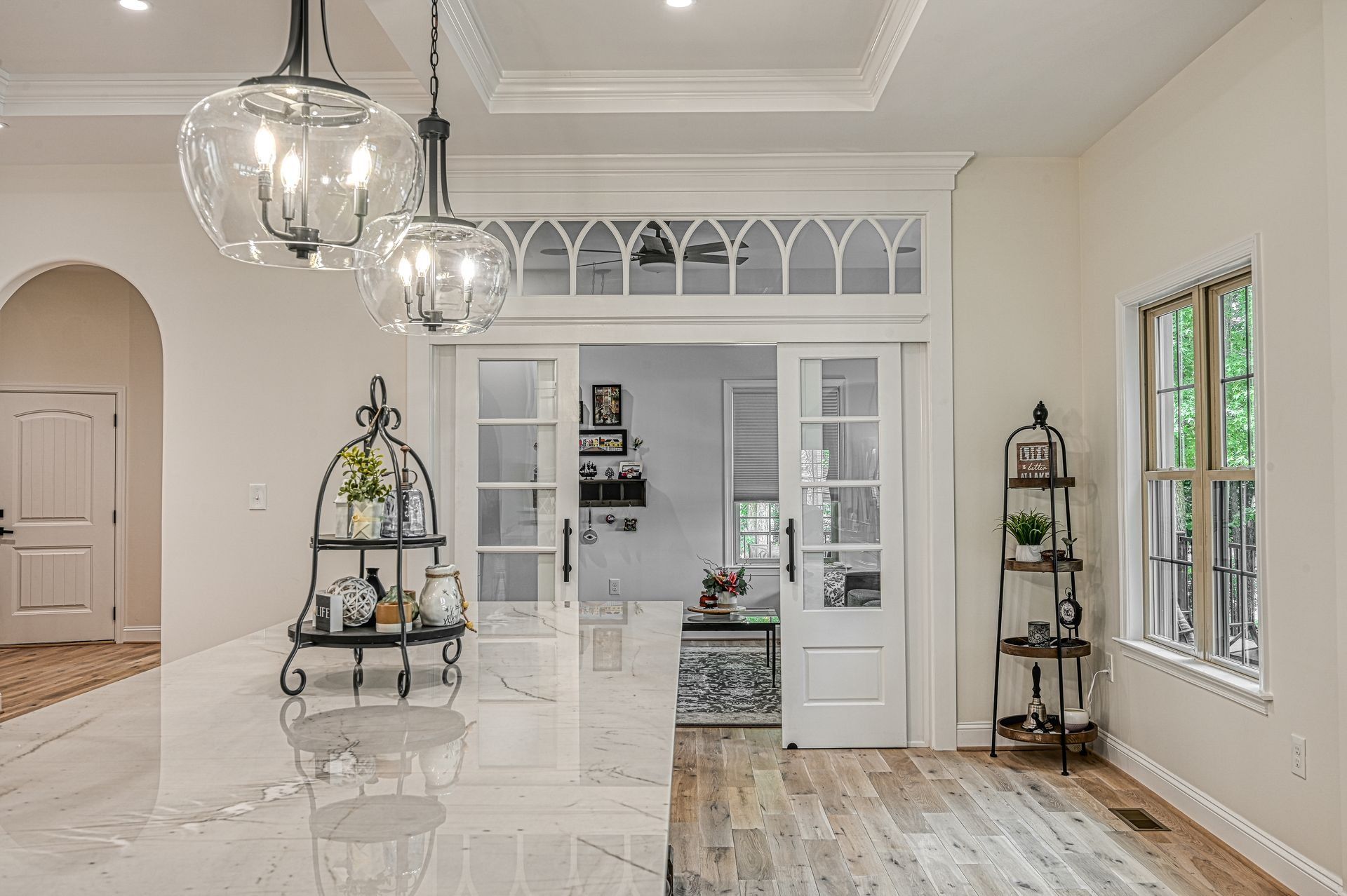 Kitchen with marble countertop, glass pendant lights, and arched doorway, leading to a room with sliding doors.