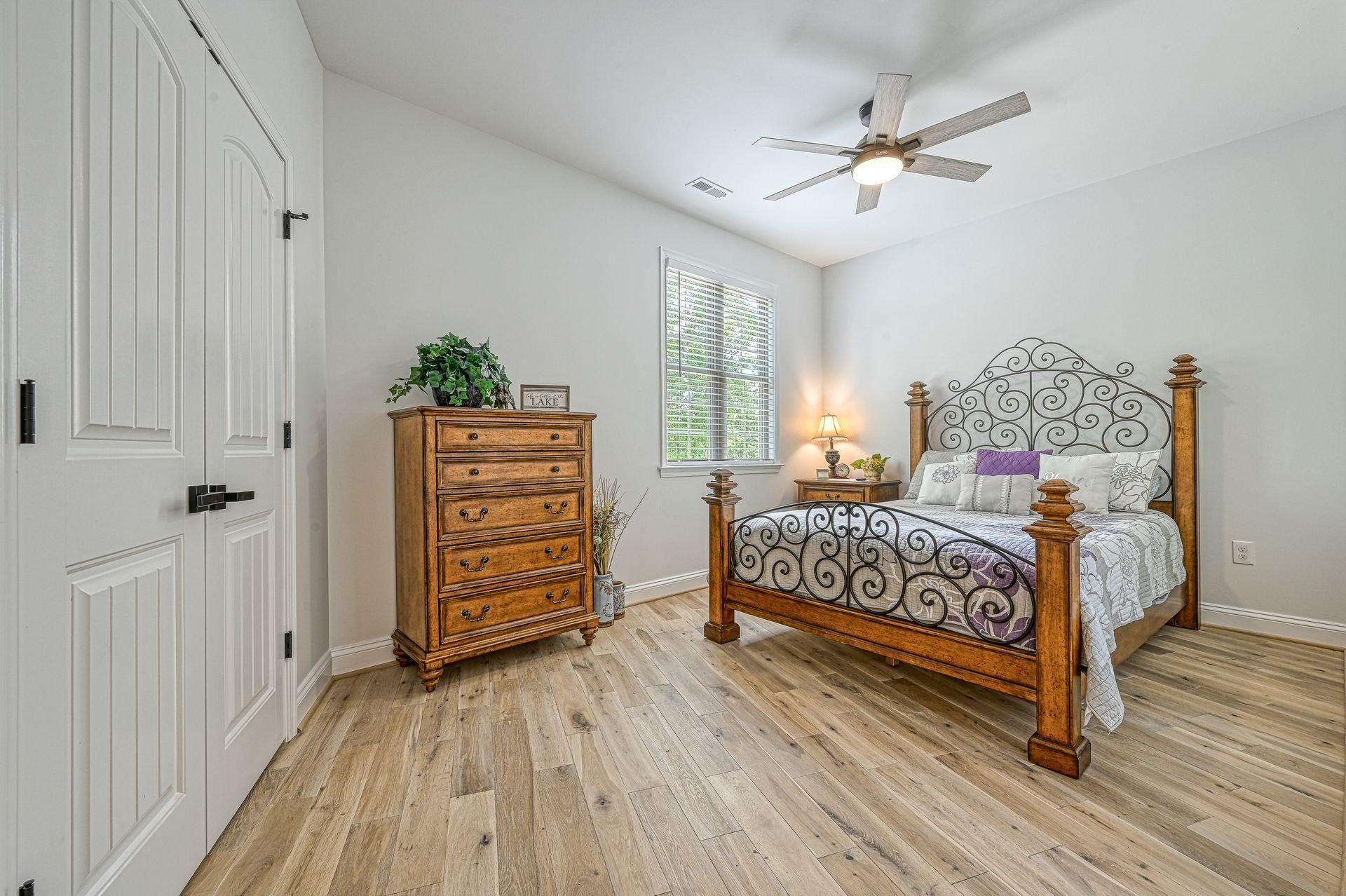 Bedroom with wooden bed, dresser, white door, and hardwood floor.