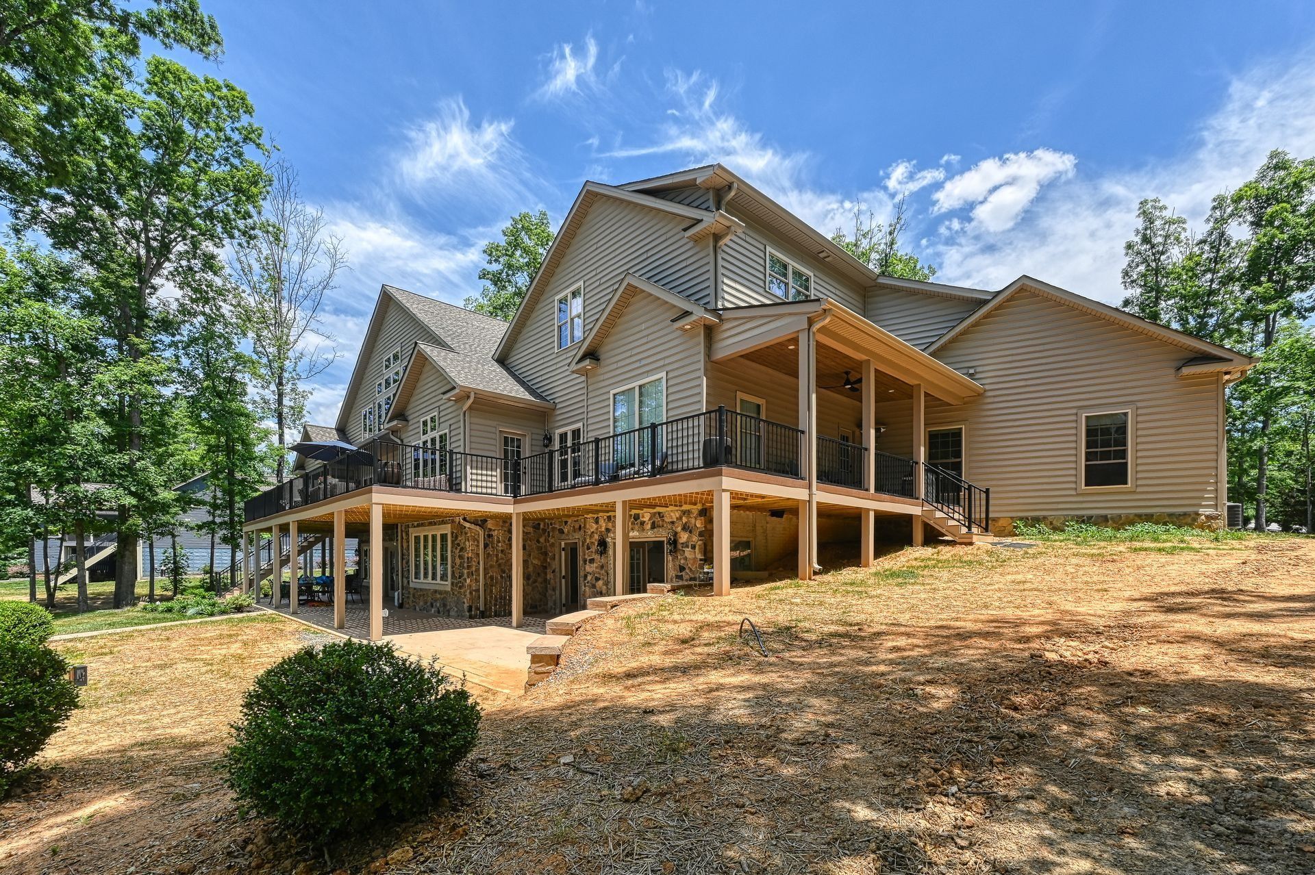 Large beige house on a hillside with multiple decks, surrounded by trees and a blue sky with clouds.