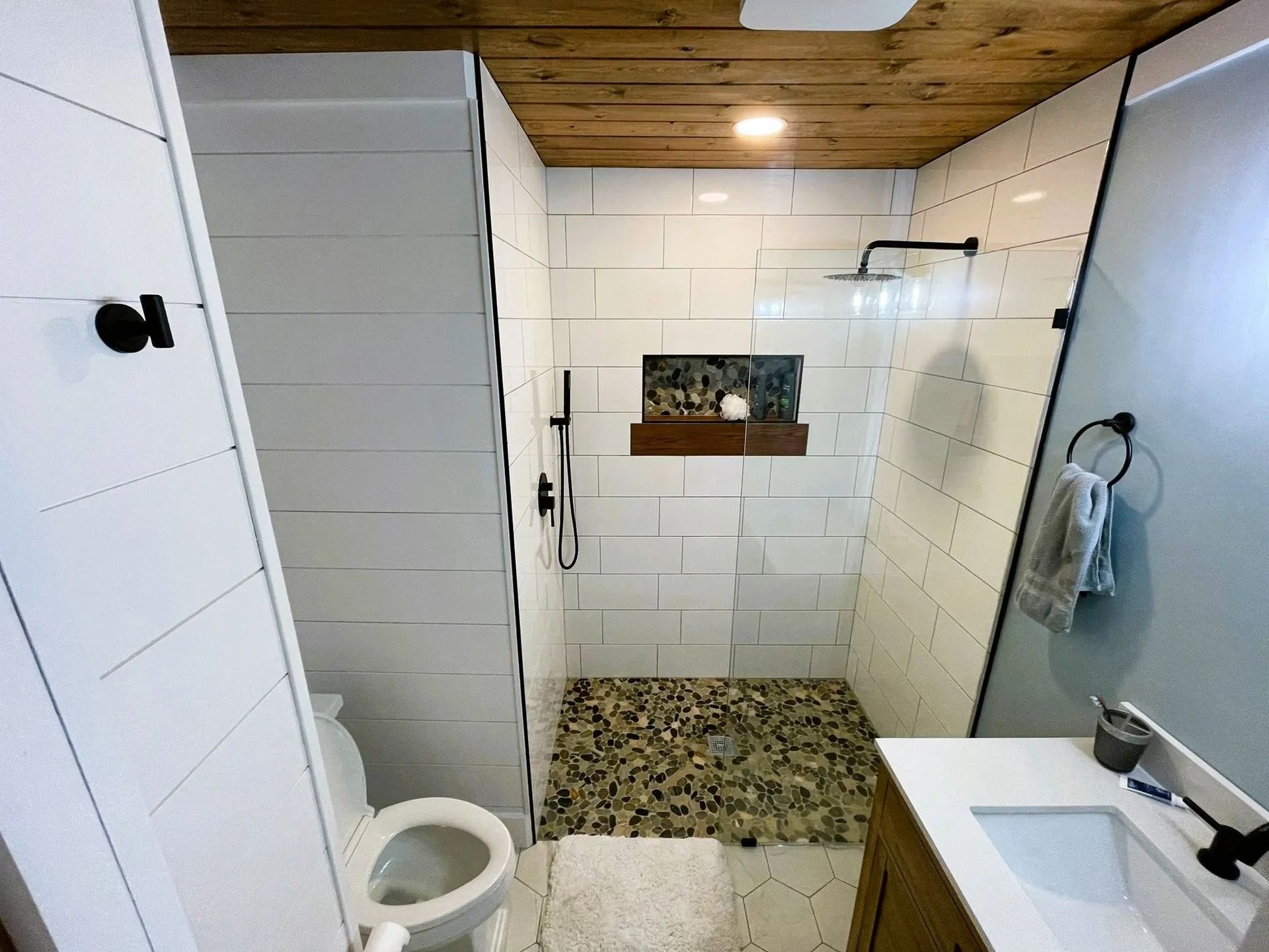 Bathroom with a tiled shower, wood ceiling, and stone shower floor. Toilet and vanity visible.