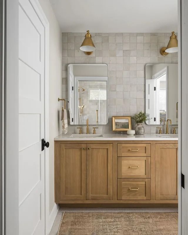 Bathroom with light wood vanity, square tile wall, and gold fixtures.