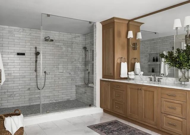 Bathroom with a glass shower, wooden vanity, marble walls, and white accents.
