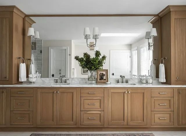 Bathroom with a long oak vanity, large mirror, and sconce lighting.