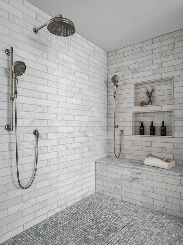 Tile shower with two shower heads, a bench, and recessed shelves.