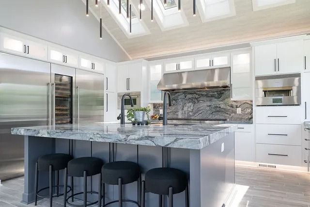 Modern kitchen with a gray island, stainless steel appliances, and gray and white cabinets.