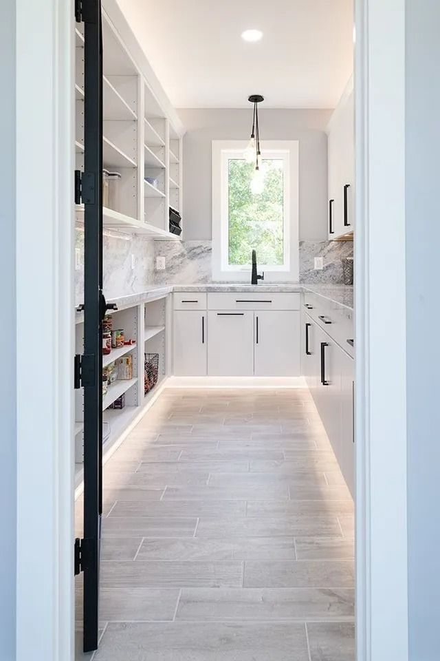 White pantry with shelves, cabinets, and a sink, lit by under-cabinet and overhead lights.