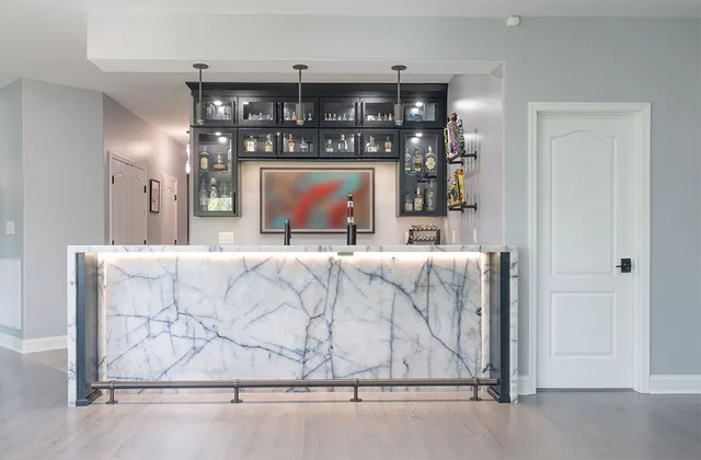 Home bar with marble countertop and dark cabinetry, under cabinet lighting, and a modern art piece.
