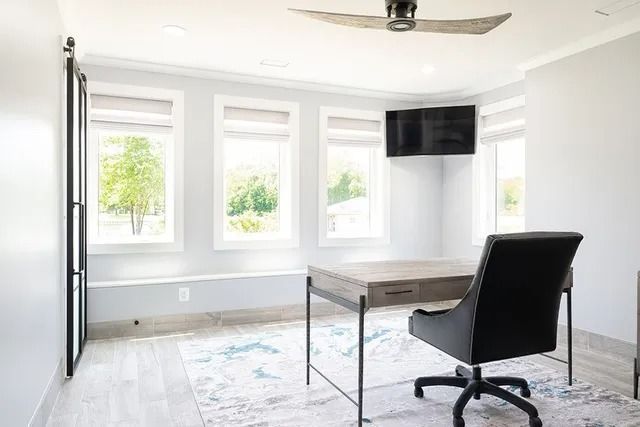 Bright office space with desk, chair, rug, windows, and mounted television.