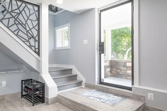 Entryway with stairs, gray walls, a decorative railing, and a black-framed glass door leading to an outdoor patio.