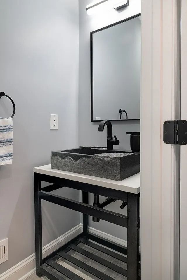 Powder room with a black stone sink, dark metal stand, and a mirror on a light gray wall.