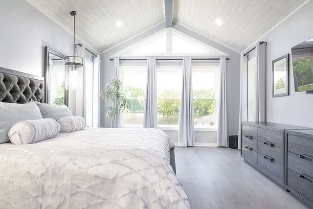Bedroom with high, angled ceiling, large windows, and gray furniture.