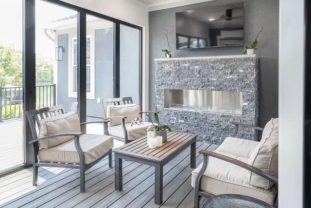 Outdoor patio with seating, fireplace, and TV. Grey stone, neutral colors, sliding glass doors.