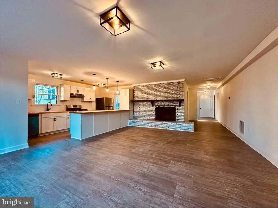 Open-concept living space with kitchen and fireplace.  Wood-look flooring, white cabinets, and neutral walls.