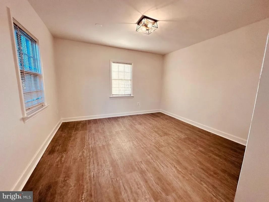 Empty room with brown flooring, white walls, and two windows.