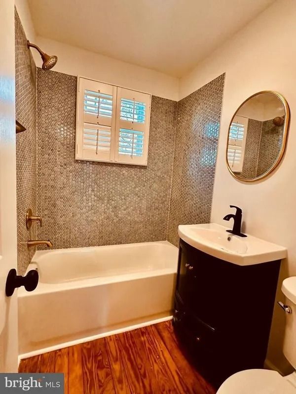 Bathroom with dark vanity, oval mirror, small mosaic tile, tub, and window.