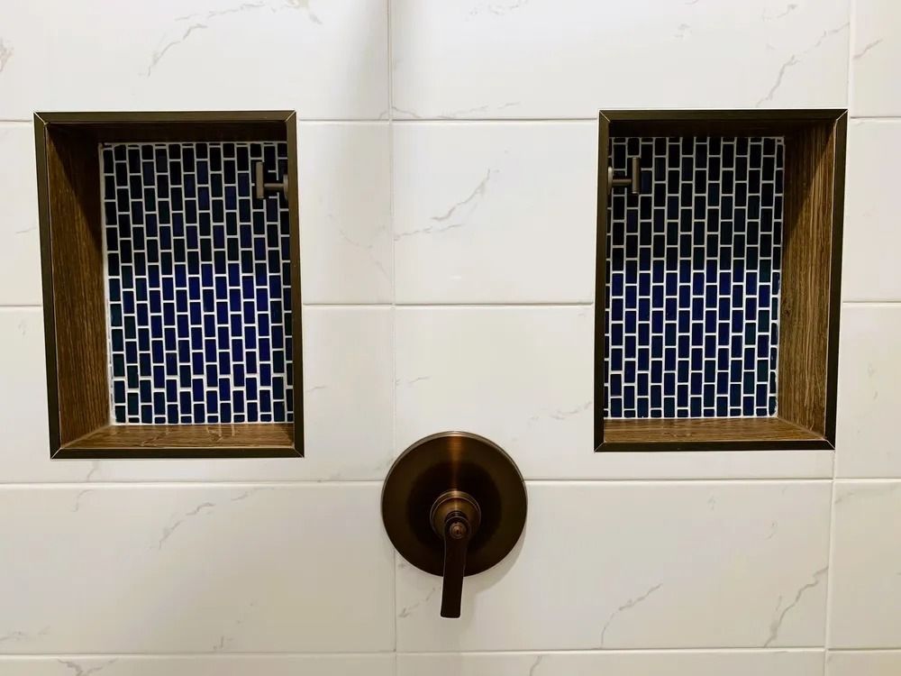 Shower wall with two rectangular inset shelves lined with blue mosaic tile; bronze faucet.